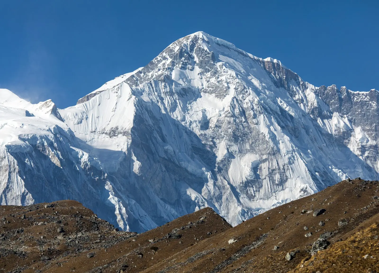 Cho Oyu, 8,201 m, the fifth highest mountain in Nepal, above brown hills under blue sky